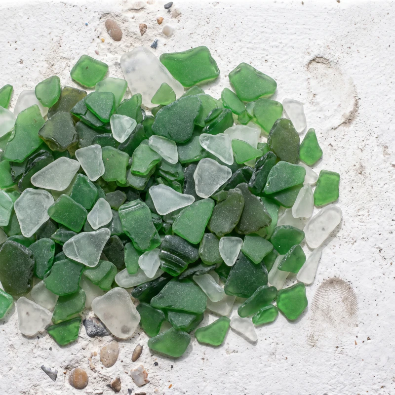 Tumbled green and clear glass chips heaped on a chalk surface