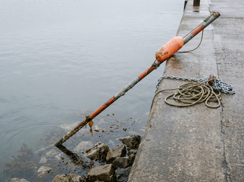 A sounding pole over a rocky ledge under shallow grey water